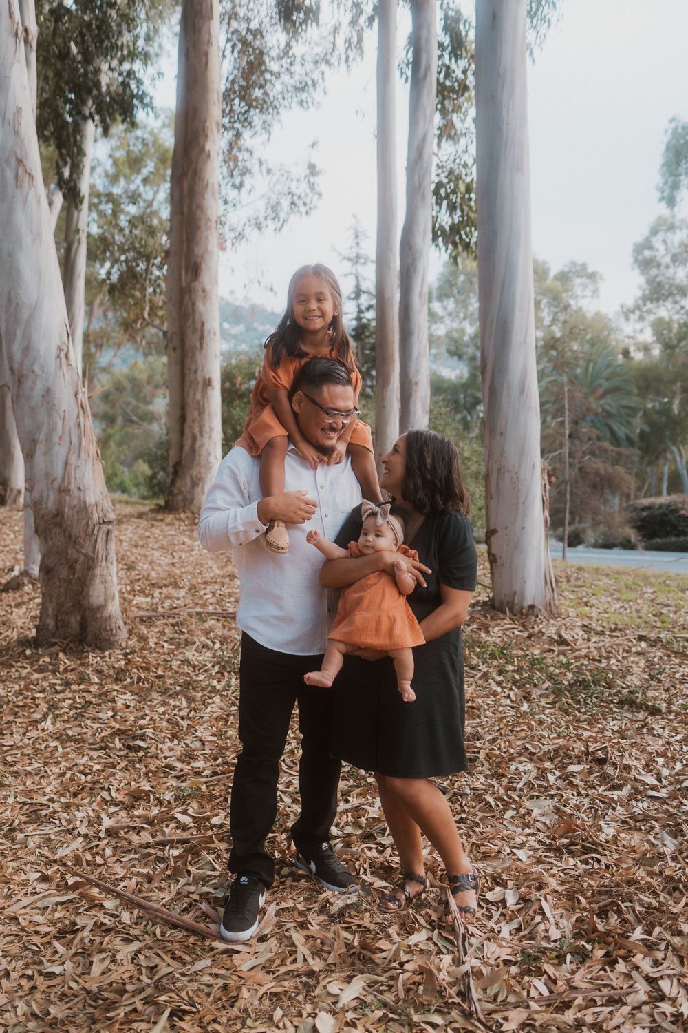 A joyful family photo session among tall eucalyptus trees with fallen leaves on the ground.
