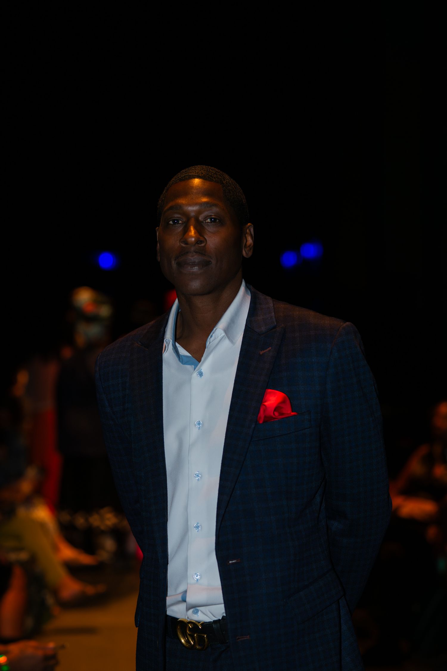 Professional wearing a navy plaid suit with red pocket square at formal event in dark setting.