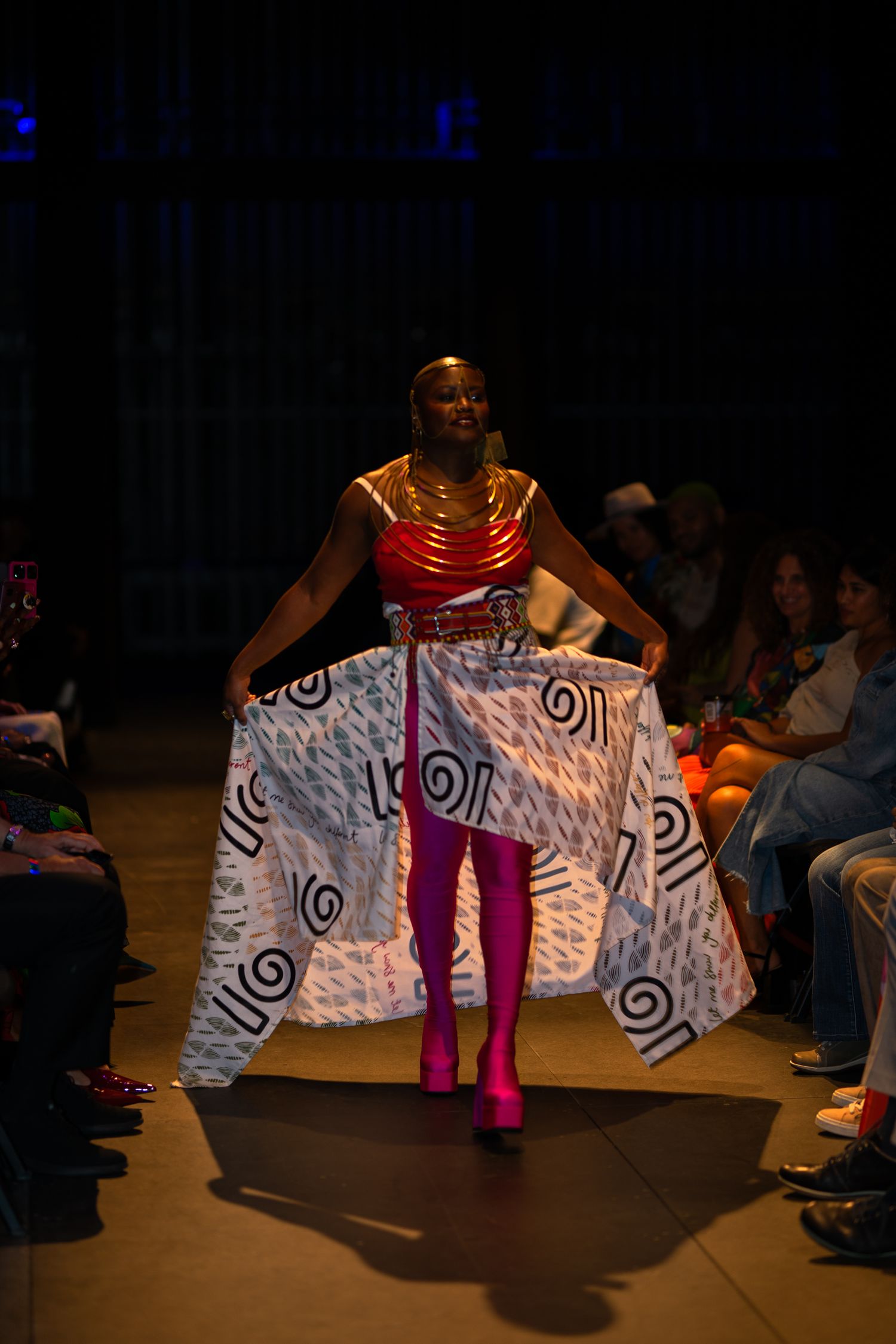 Model showcasing spiral-patterned dress with hot pink boots on fashion runway.