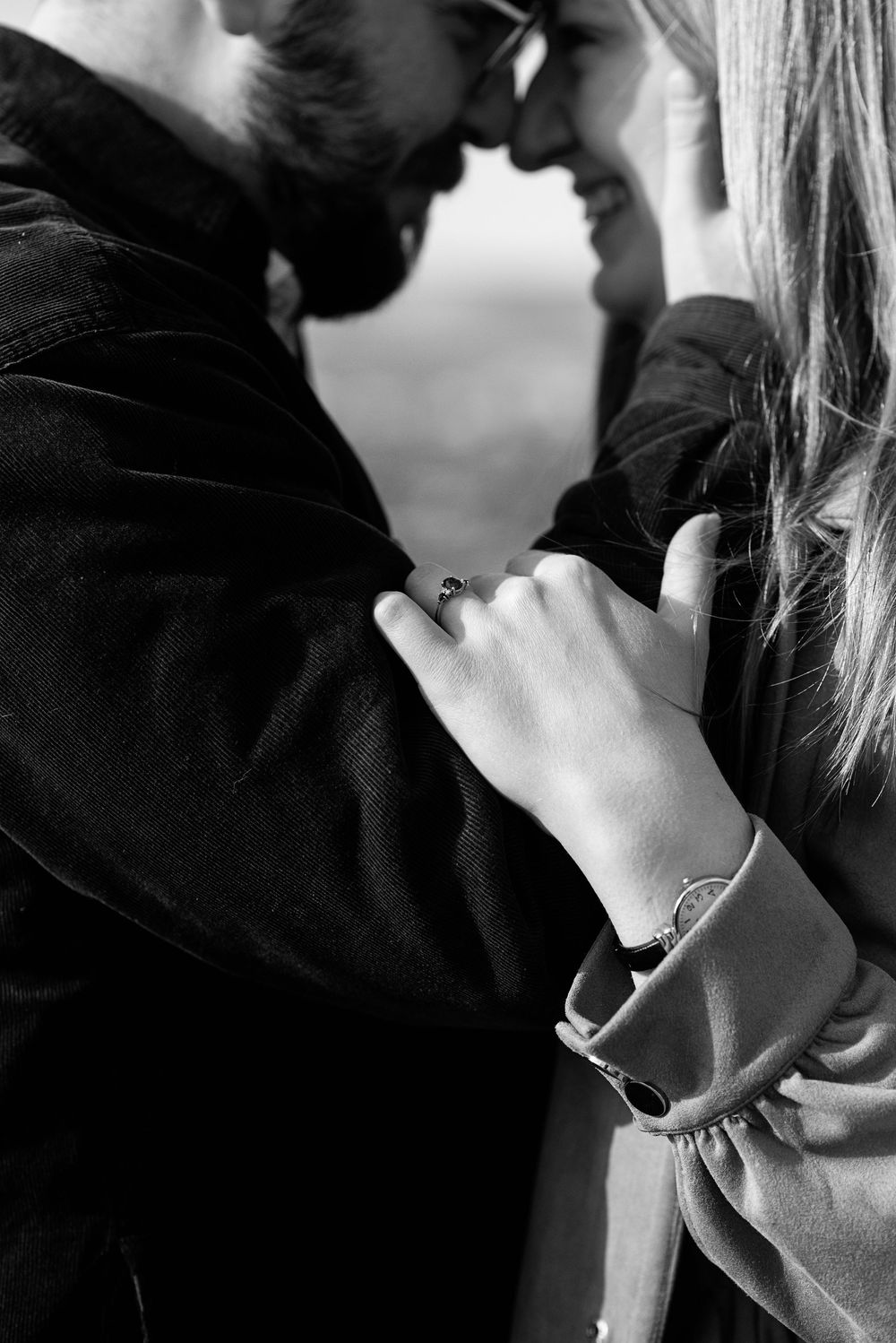 Black and white photo of a couple embracing closely, woman wearing a ring resting her hand on mans chest.