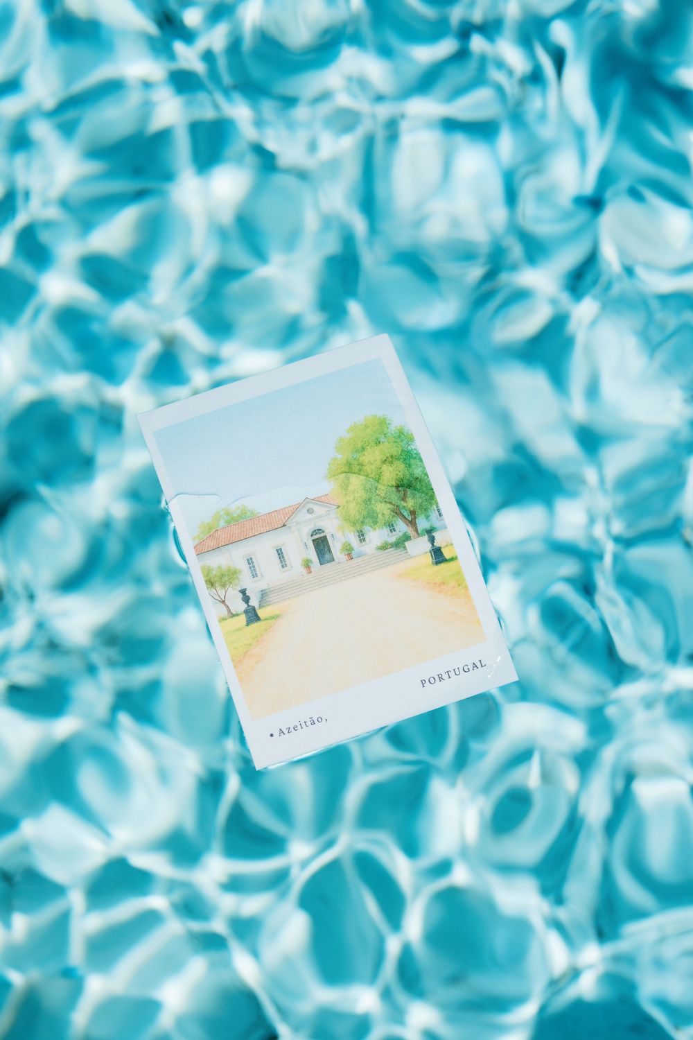 Two artistic watercolor postcards float on rippling turquoise pool water creating a dreamy summer vacation scene.