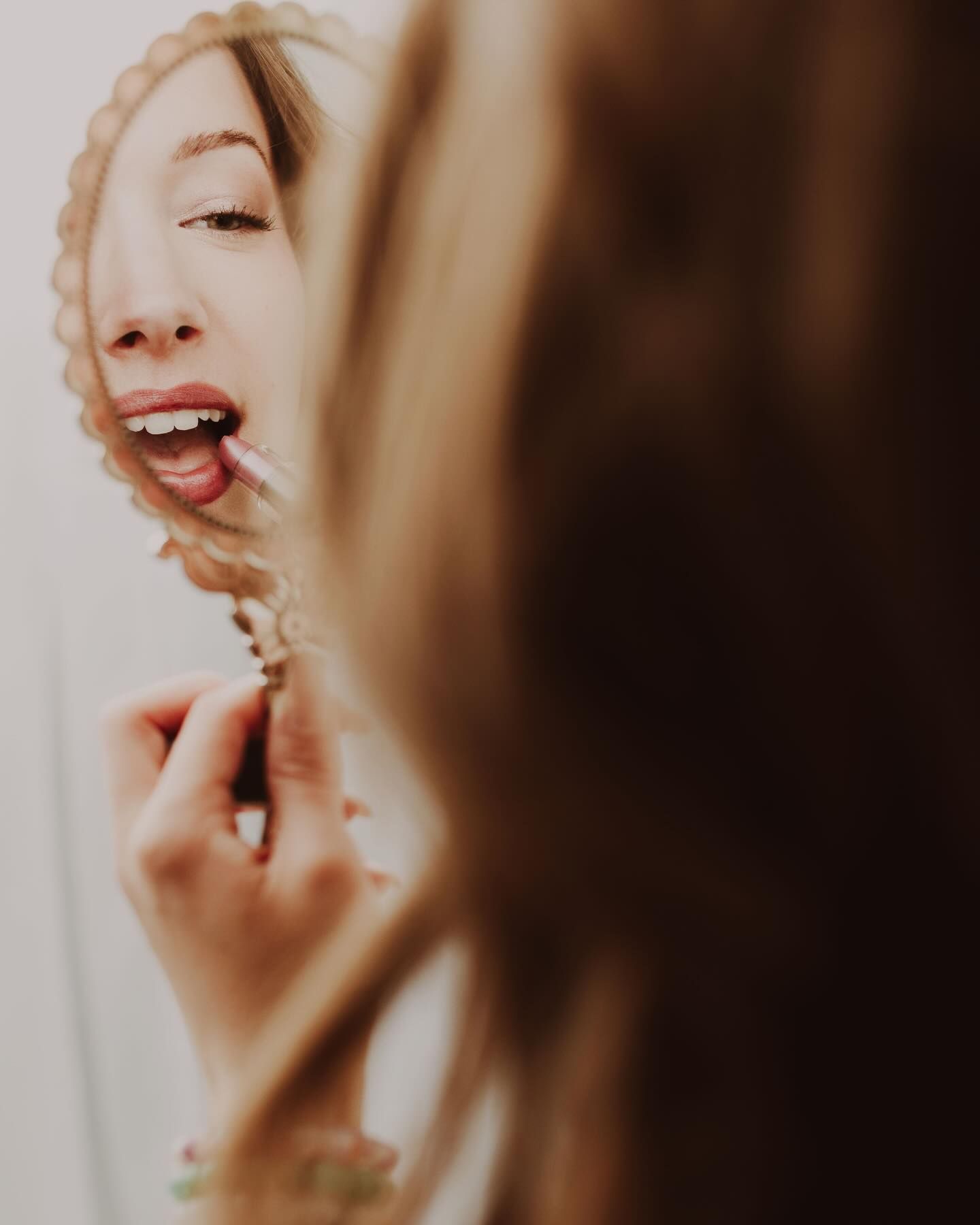 Reflection in mirror shows a joyful expression with closed eyes and bright smile in warm lighting. Elizabeth Lang Photography Surrey