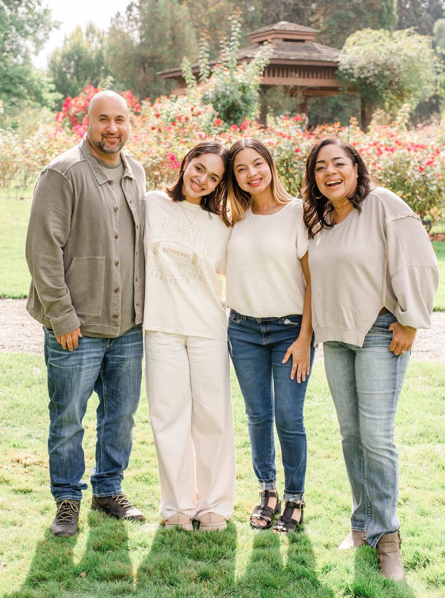 A group of four people in casual clothing pose together outdoors in a garden with blooming flowers and greenery.