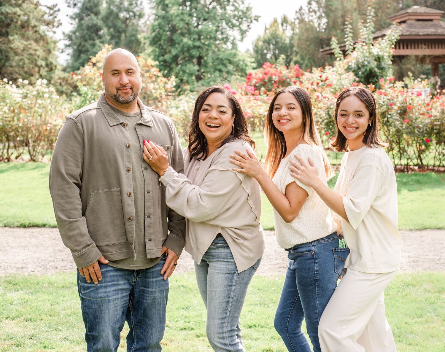 A cheerful group poses playfully together in a sunny garden setting with red flowers and greenery.