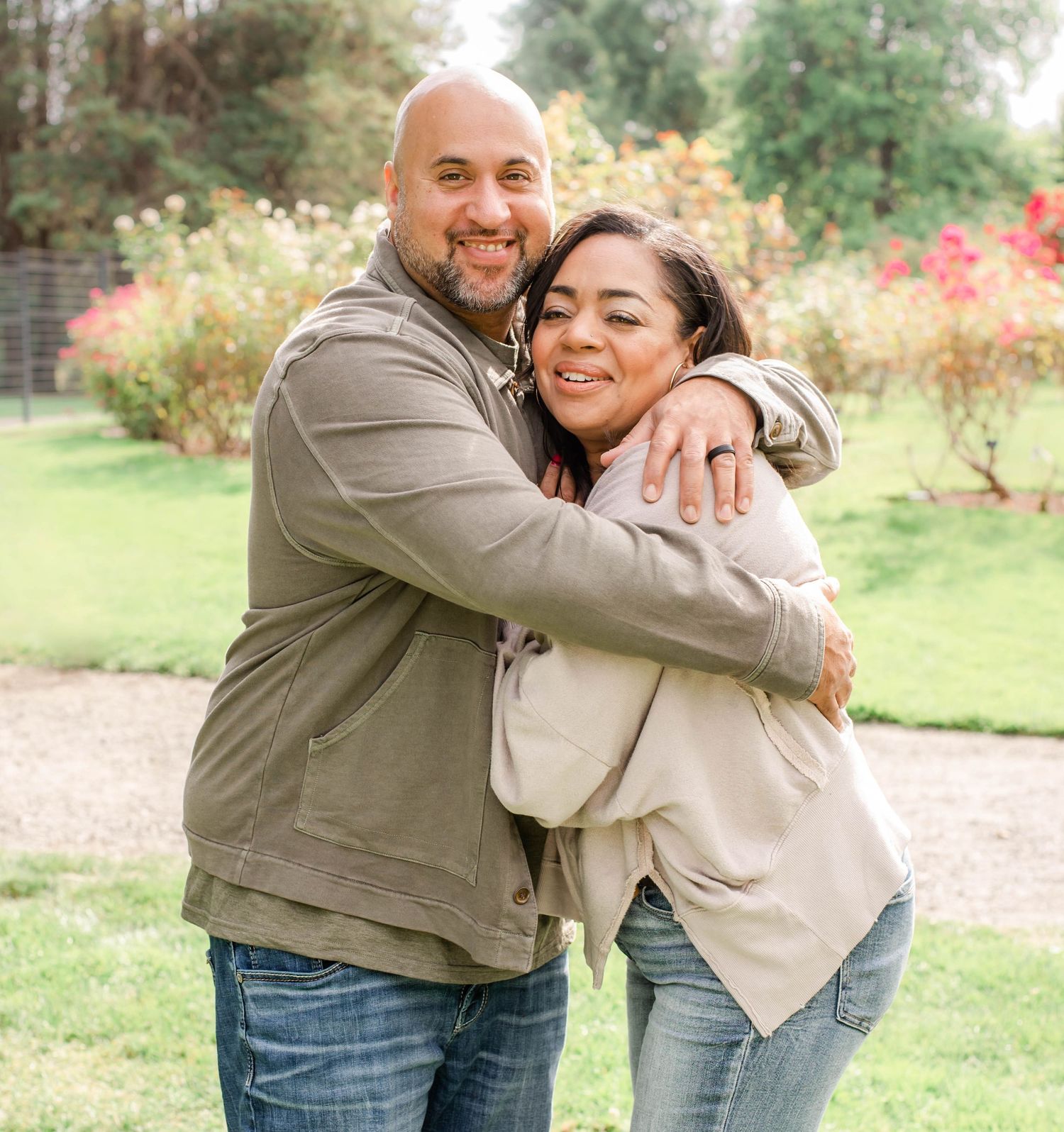 A happy couple embraces outdoors in a park with autumn foliage and greenery in the background.