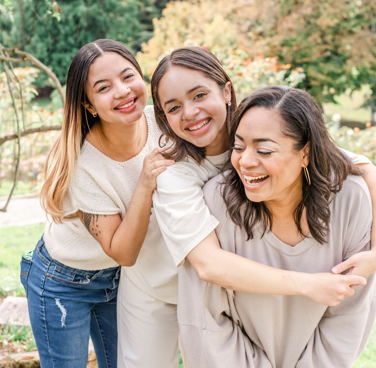 Three friends in neutral-colored clothing share a genuine moment of laughter in an outdoor setting.