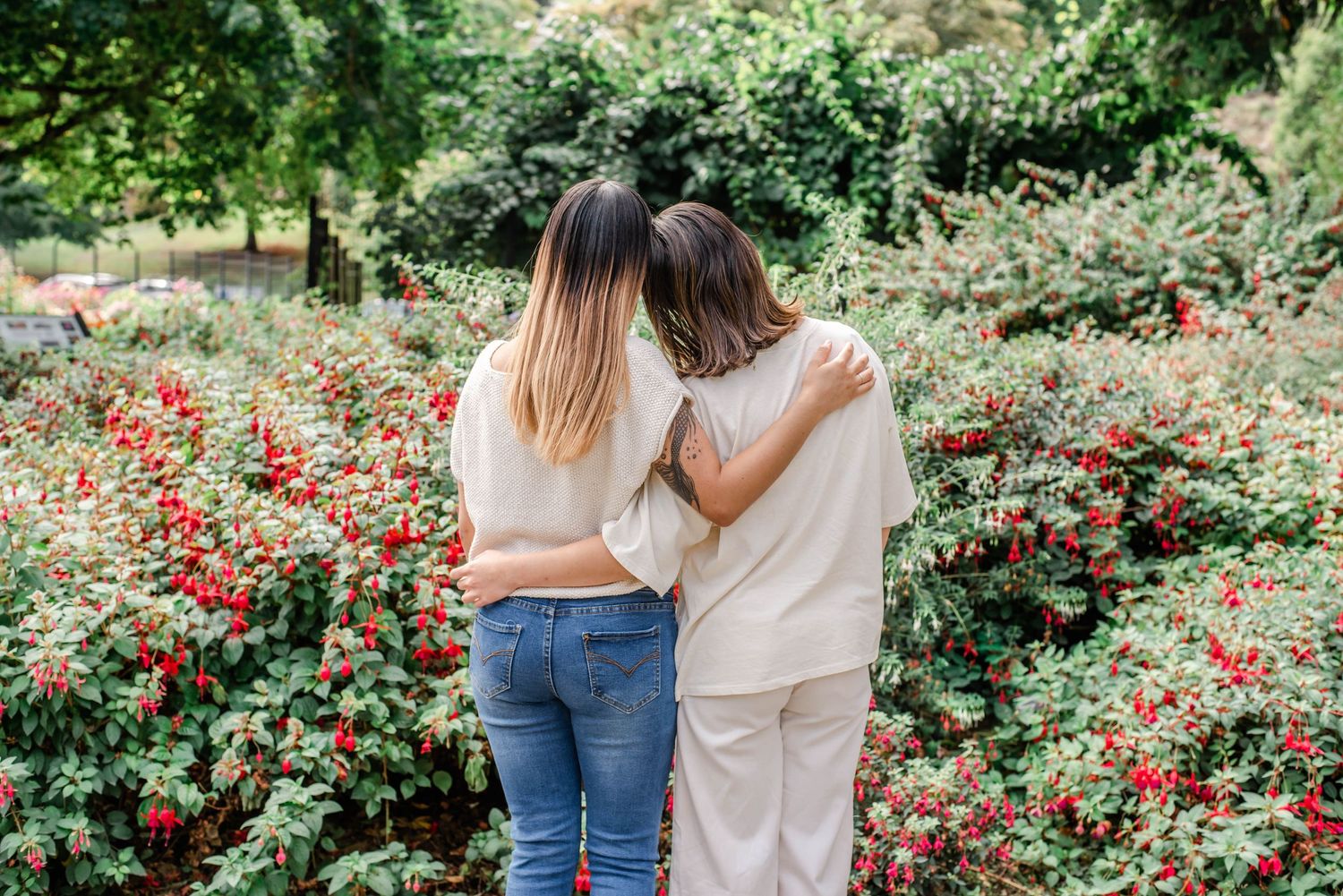 Friends posing playfully together in a garden with blooming red flowers and greenery in the background.