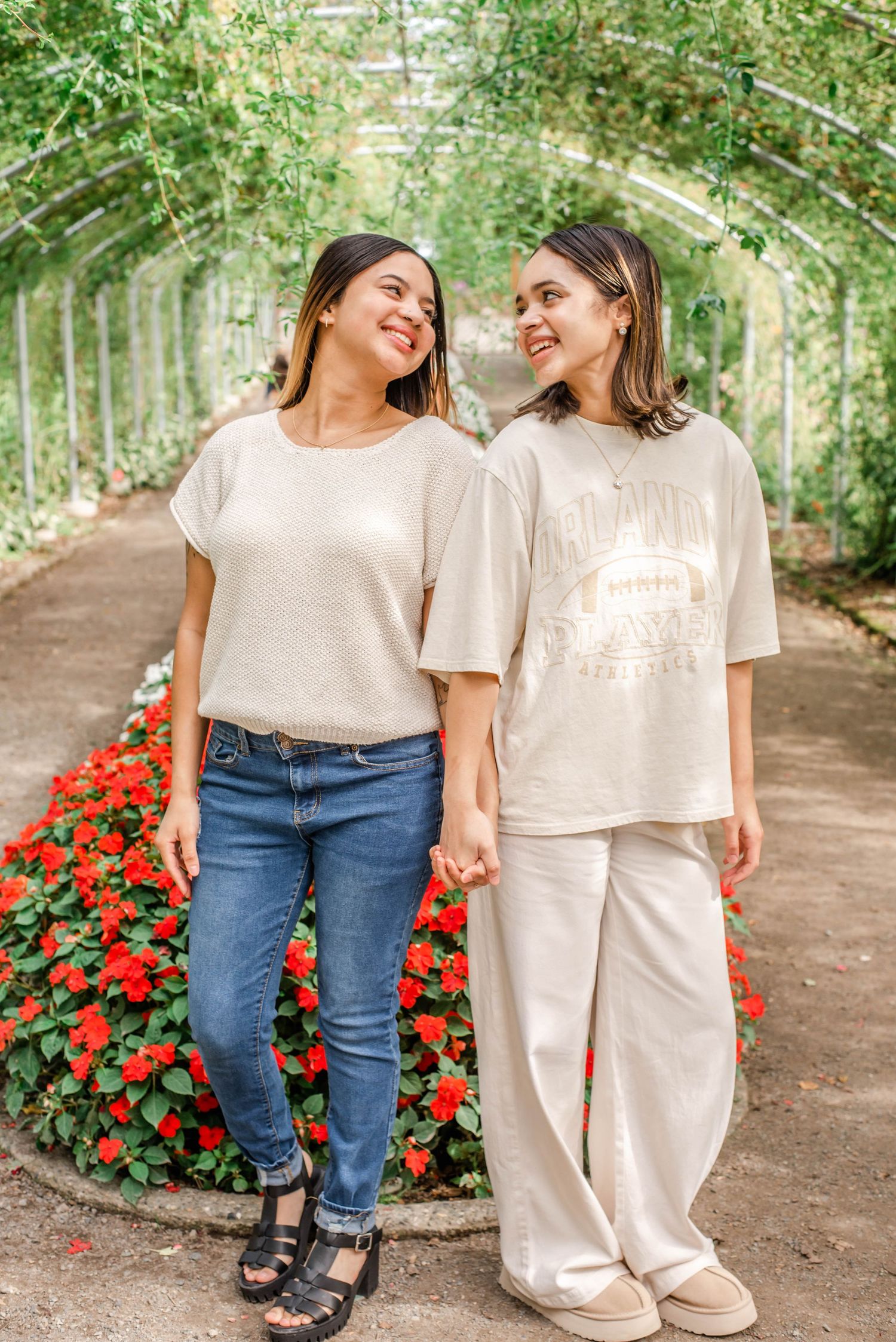 Family members in matching cream-colored tops and jeans walk together along a garden path with red flowers.