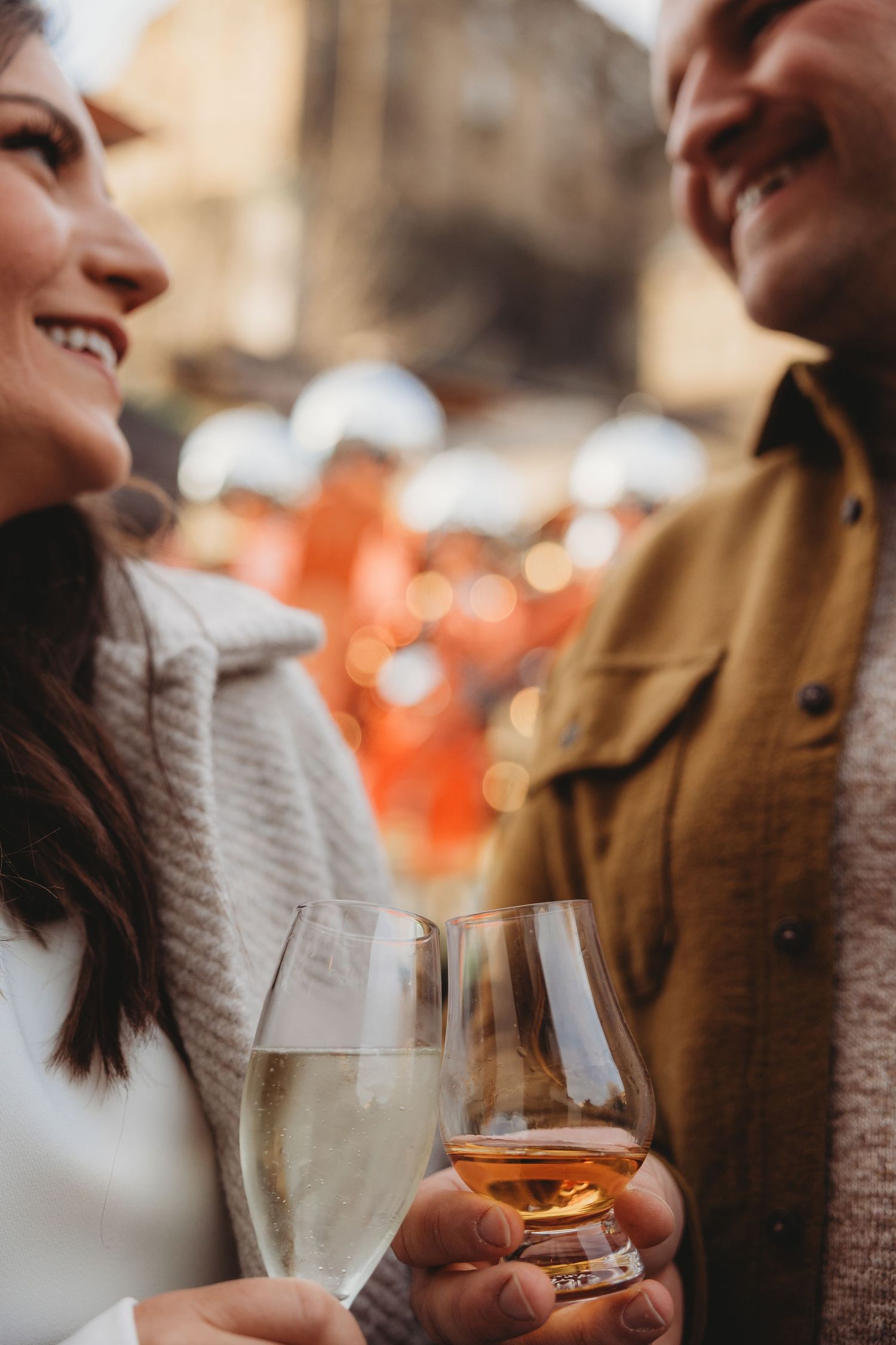 Two people share drinks and conversation at a cozy bar with warm lighting and bokeh effects in the background.