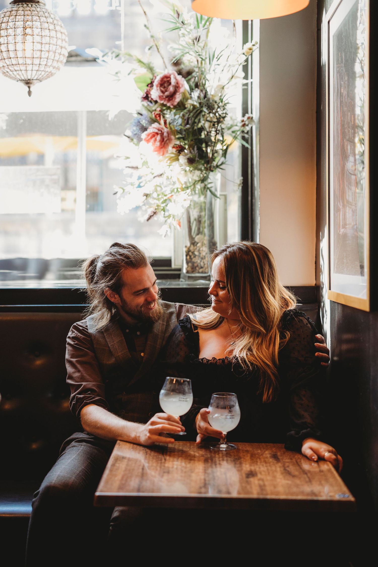 Romantic couple enjoying drinks together at a cozy restaurant with floral decor and warm lighting.