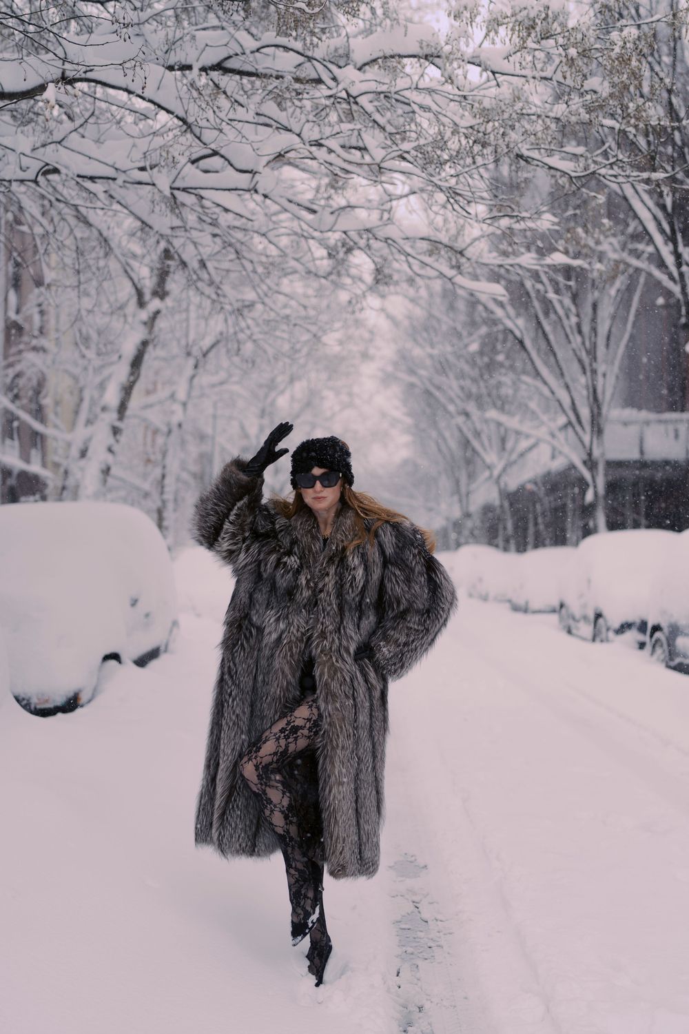 A person in a luxurious fur coat walks through a snow-covered path lined with frost-covered trees in winter.