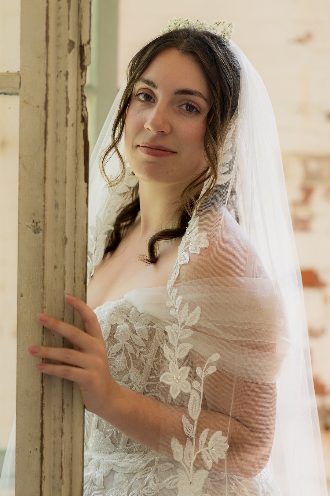 Frederick Maryland Wedding Photographer Bride in delicate lace veil poses elegantly by vintage window frame.