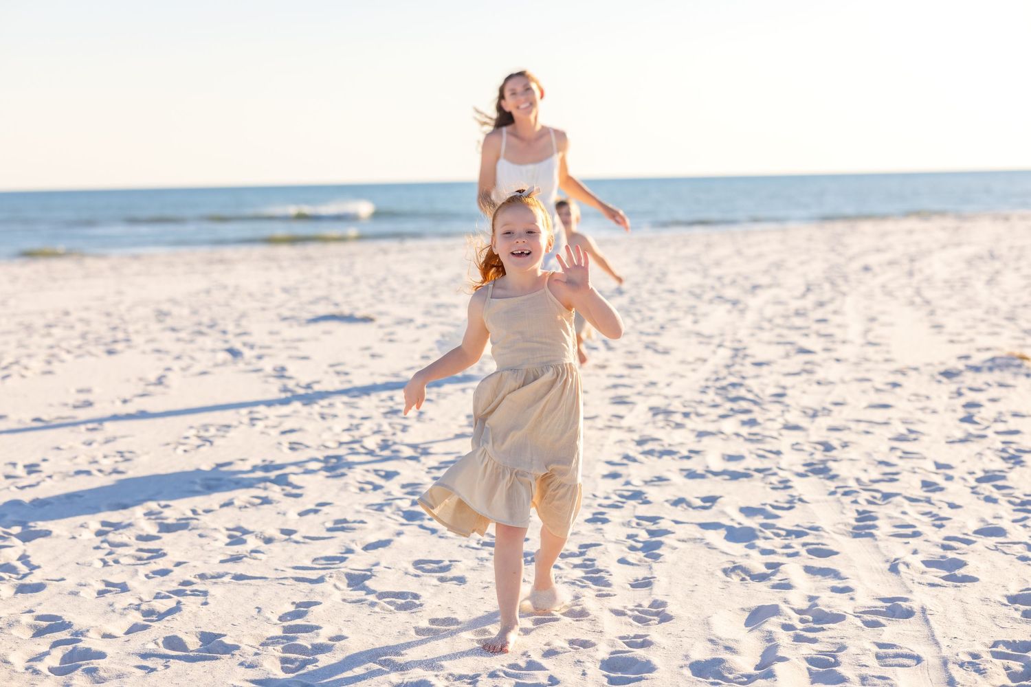 Children play and run along a pristine white sandy beach on a bright sunny day at the ocean shore.