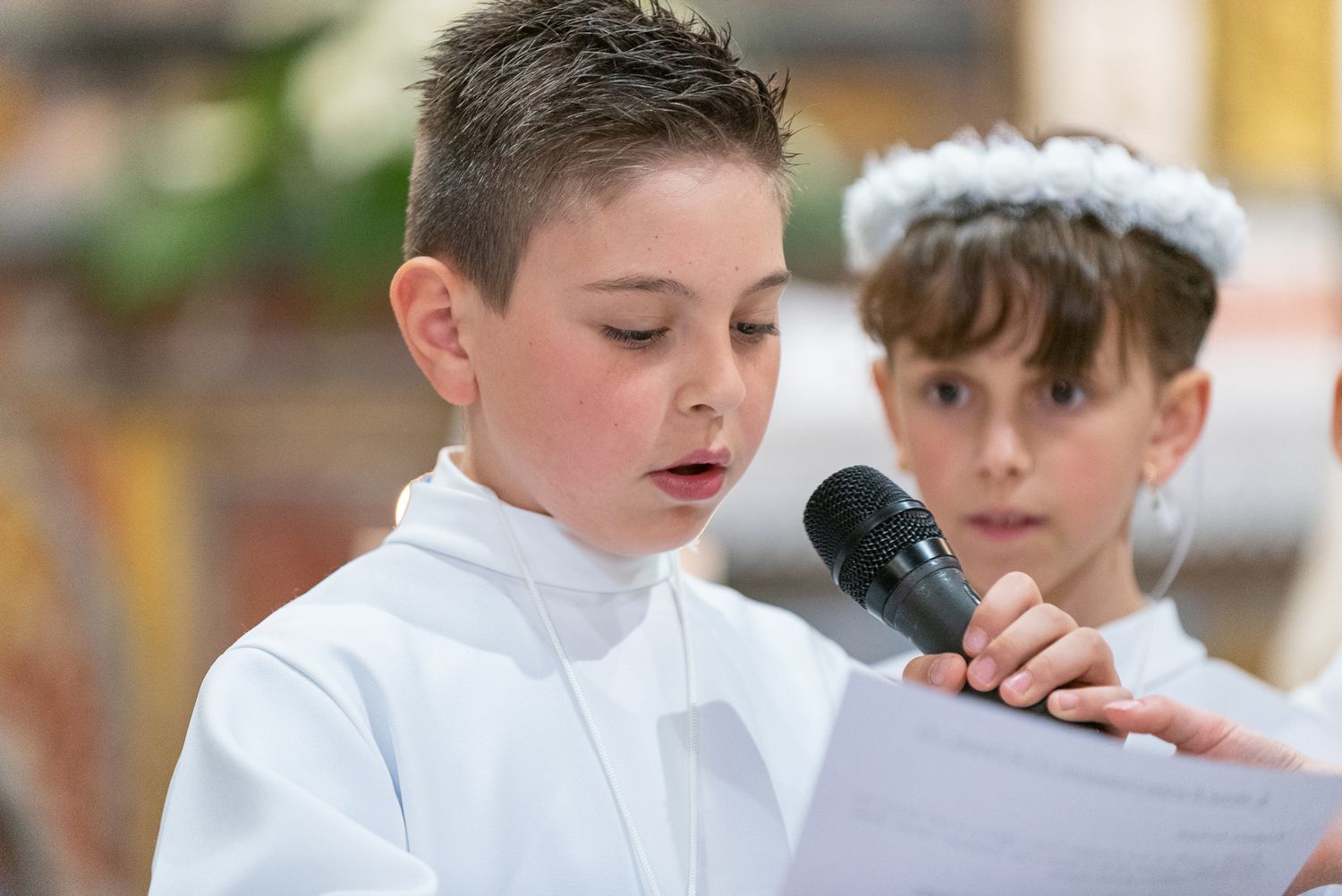 Young person in white robe speaking into microphone during church service.