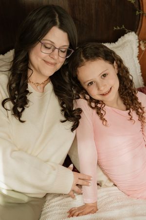 A tender moment shared between parent and child in matching white and pink outfits as they cuddle together on a couch.