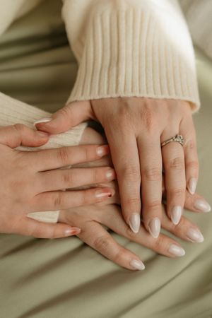 Close-up of hands with neutral manicured nails and engagement ring resting on cream-colored fabric.