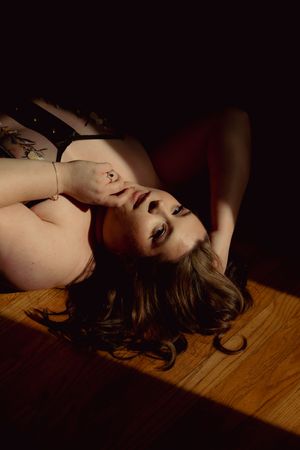 Artistic boudoir photography series showing a figure reclining on wooden flooring in dramatic lighting.