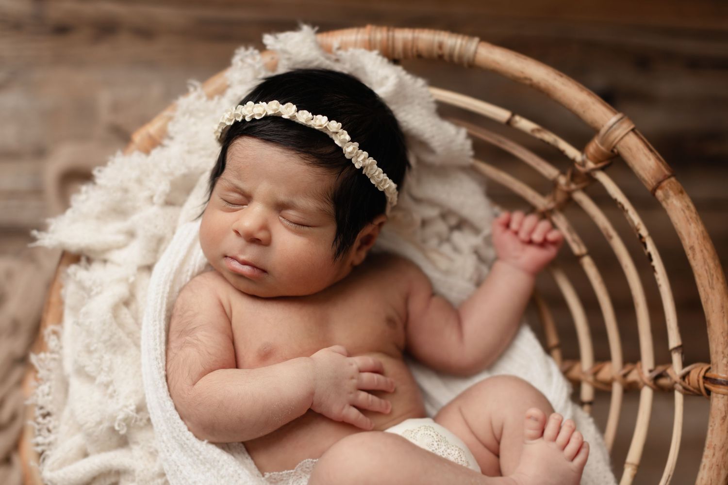 Newborn baby sleeping peacefully in a wooden bowl with white blanket and delicate lace headband. Elizabeth Lang Photography Surrey