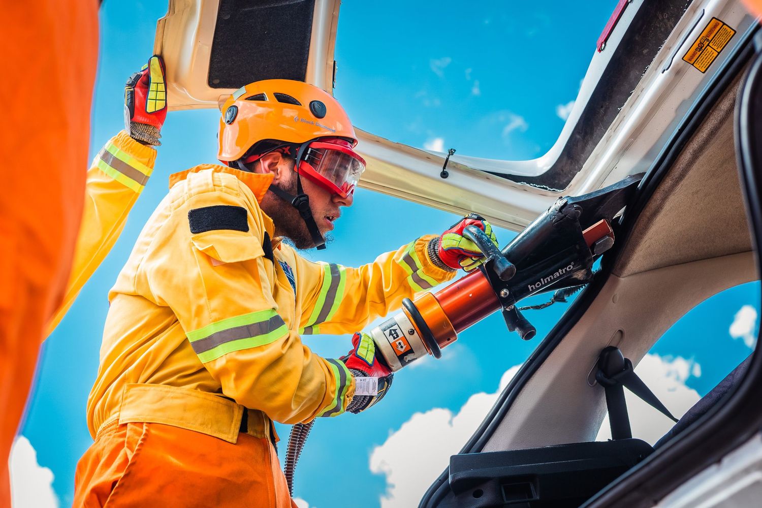 Firefighters in protective gear and helmets work together during an emergency response operation against bright blue sky.
