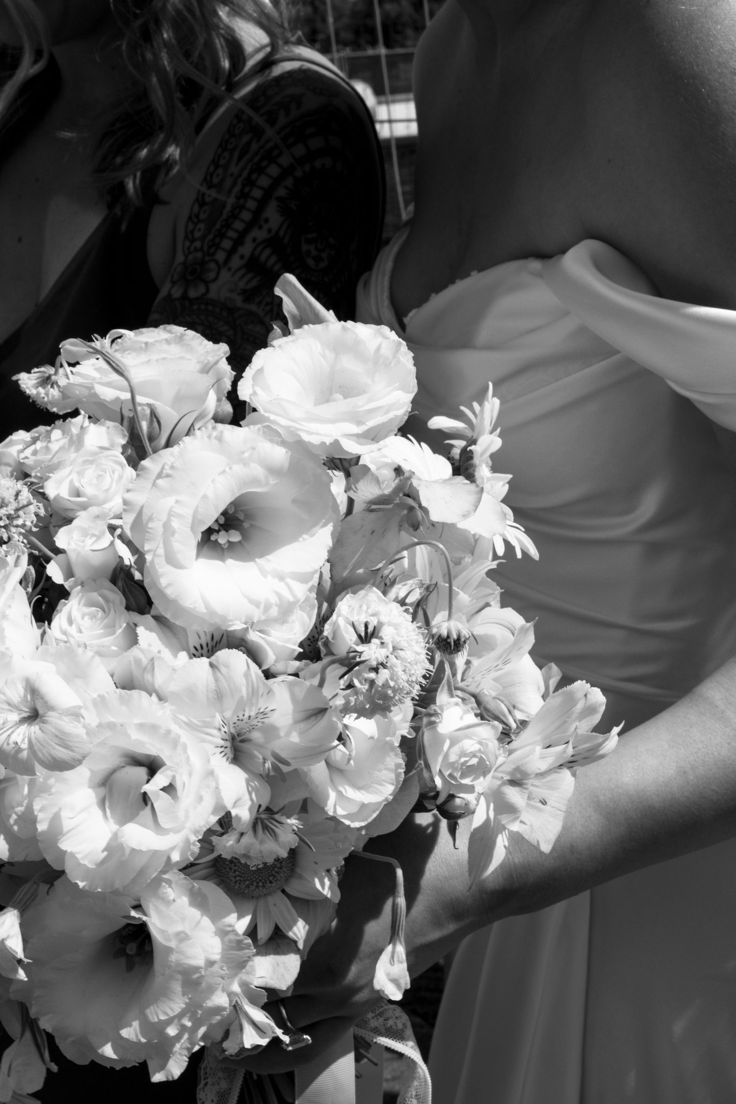A black and white photograph of an elegant white bridal bouquet with lush roses and lilies held against a flowing gown.