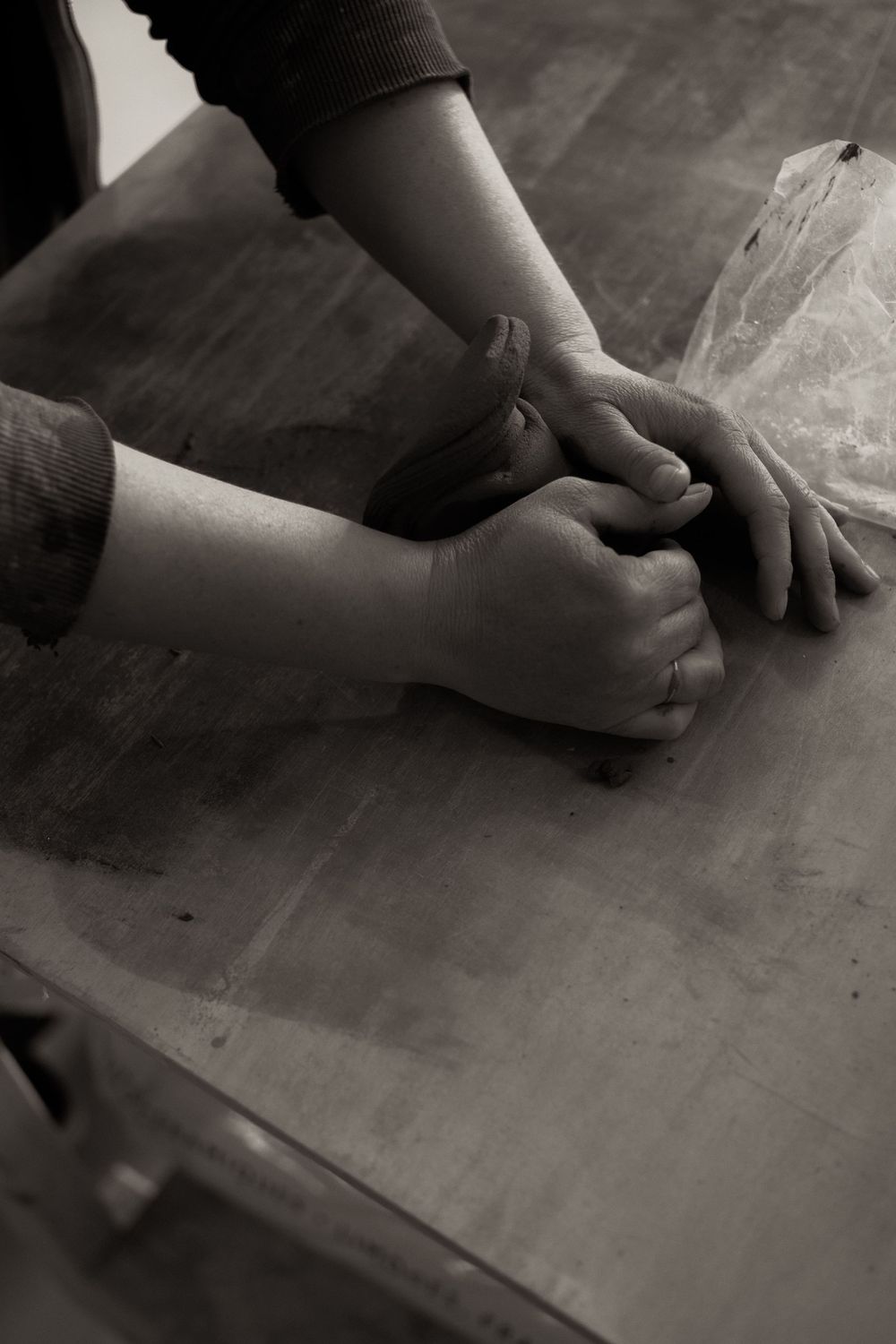 Black and white photo of hands kneading dough on a wooden table surface.