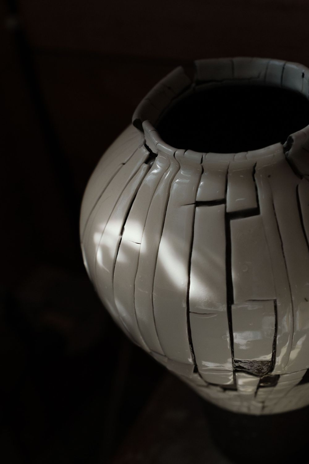 A cracked white ceramic vase with a mosaic-like pattern, dramatically lit against a dark background.