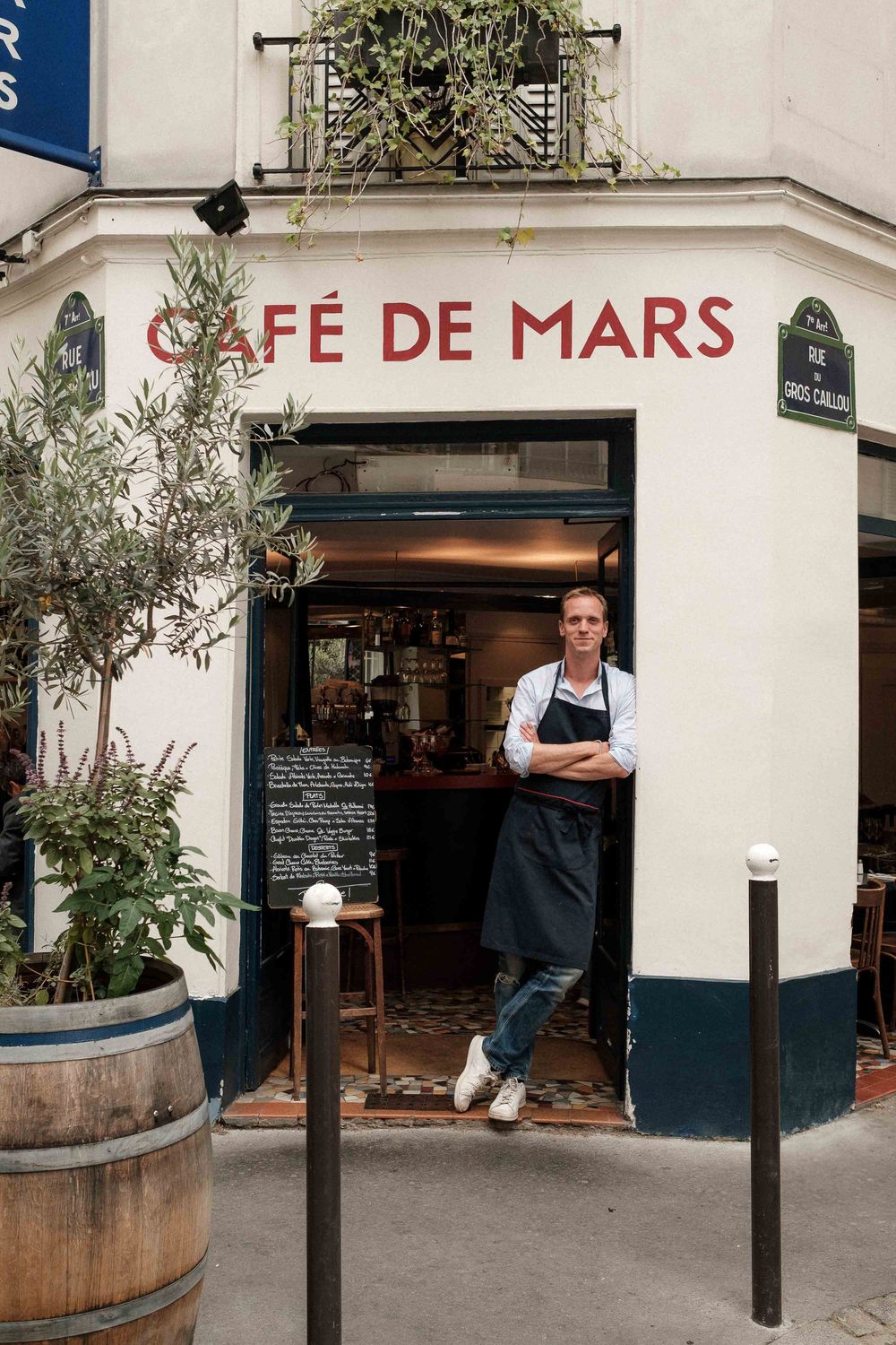 Exterior view of Cafe de Mars restaurant in Paris with black poles and wine barrel outside the entrance.
