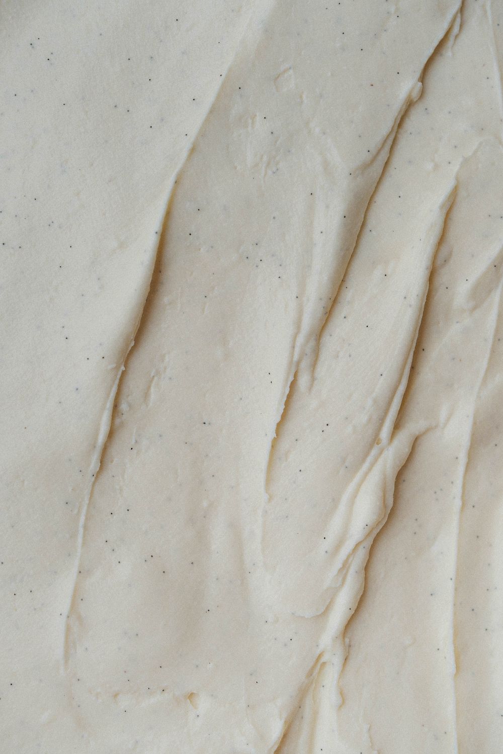 Close-up texture of smooth white frosting or cream with gentle ripples and folds creating an elegant surface pattern.