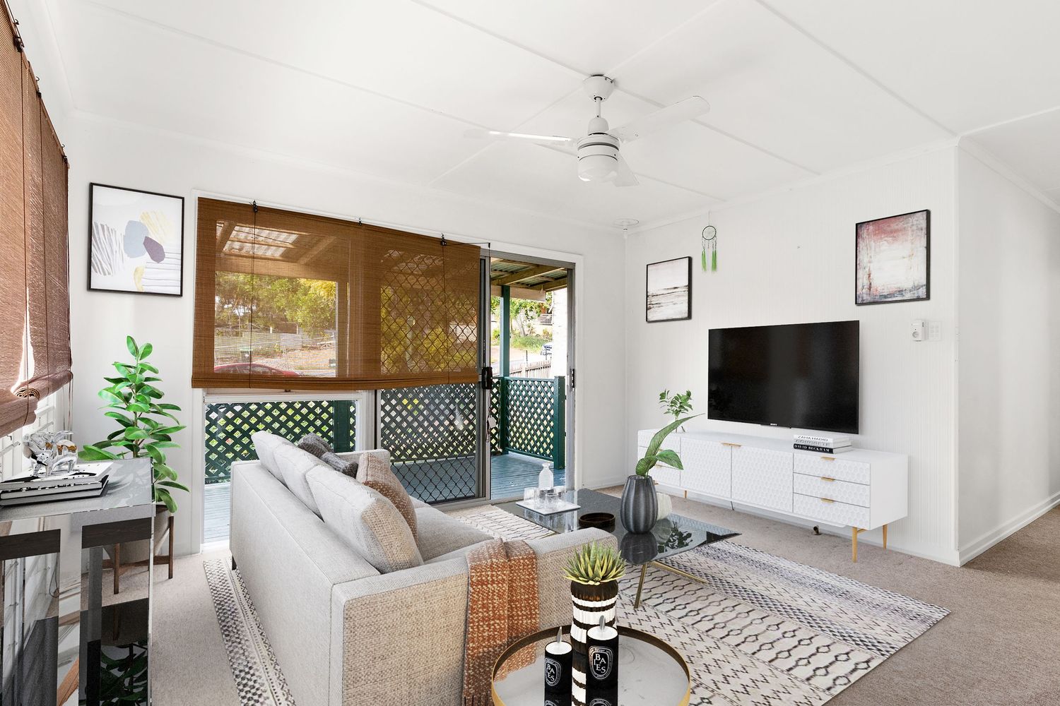 Cozy living room with neutral sofa, ceiling fan, bamboo blinds, and sliding doors opening to an outdoor area.