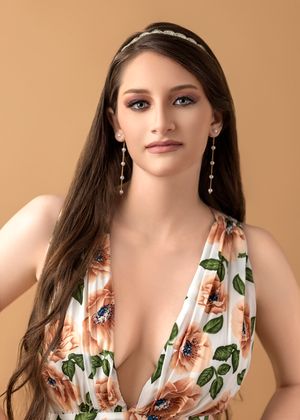 Portrait of a model wearing a floral v-neck dress with long dark hair, crystal headband and dangling earrings.