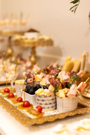Elegant catering display of gourmet appetizers and canapes arranged on gold platters with decorative paper holders.
