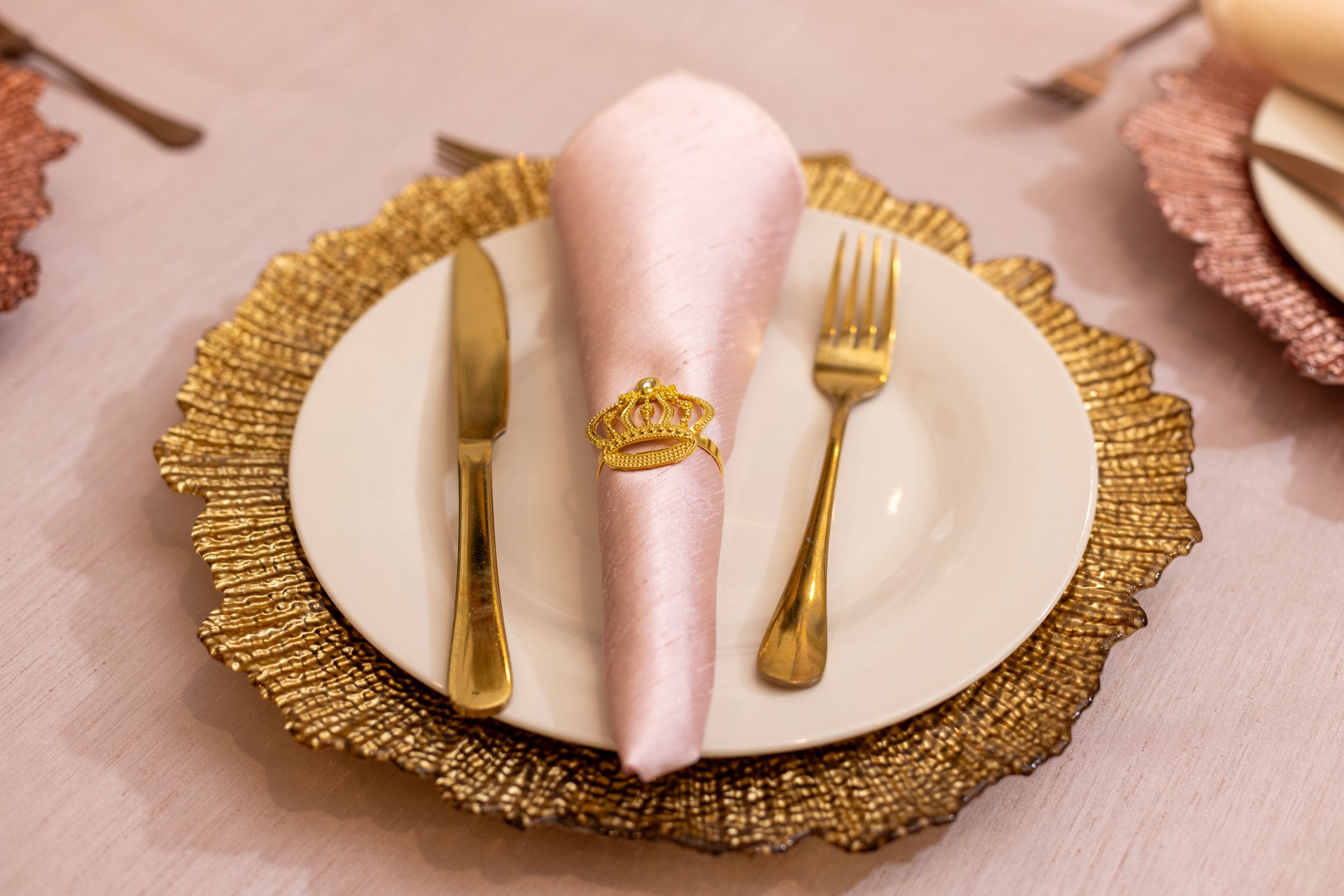 Gold charger plates with elegant flatware and pink napkins create an upscale table setting for a formal dinner party.