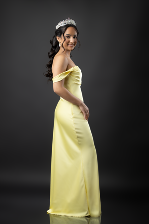 Pregnant woman in flowing yellow gown poses elegantly against dark background in maternity photoshoot series.