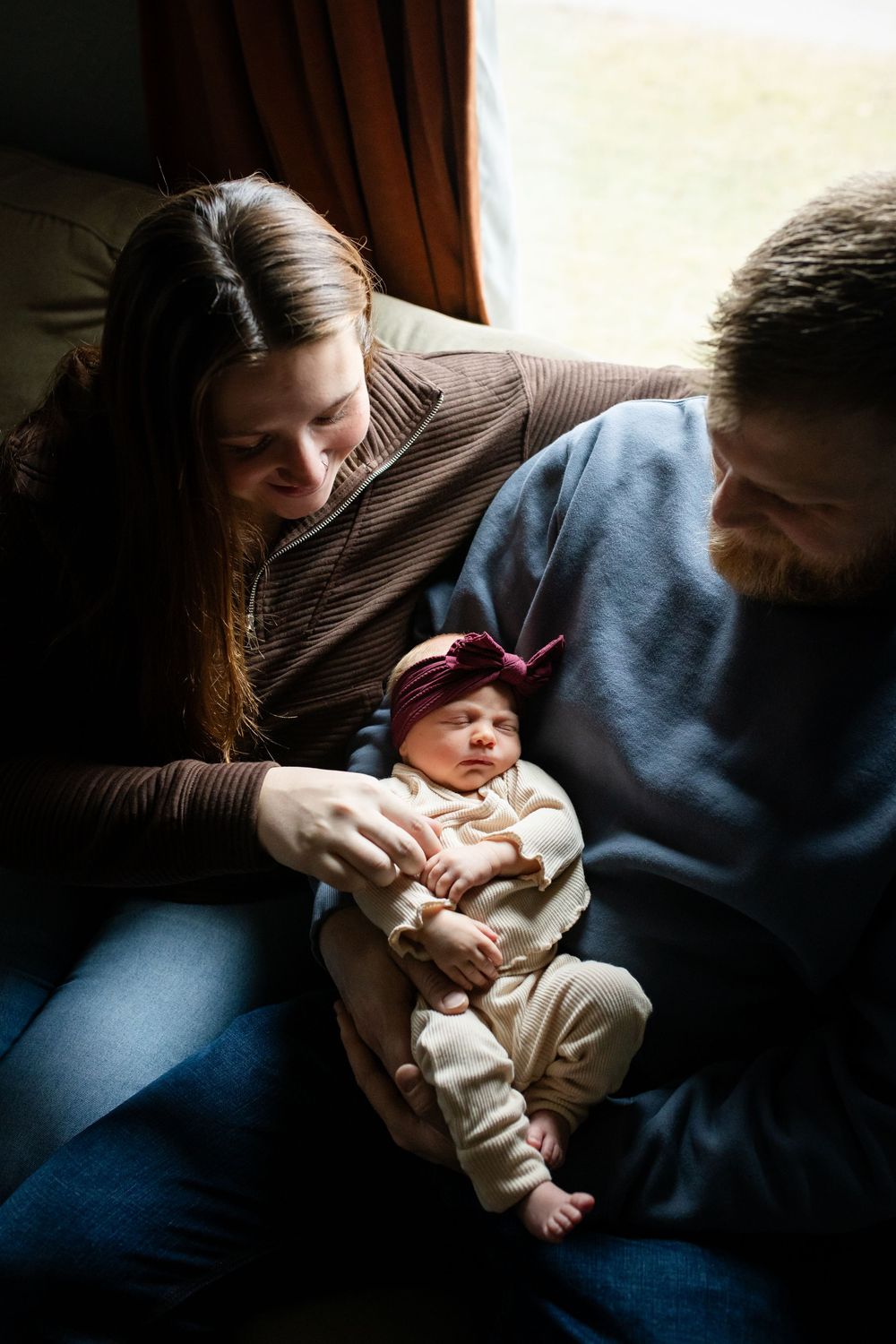 A series of intimate photos showing a parent holding and bonding with a newborn baby on a blue couch in dim lighting.