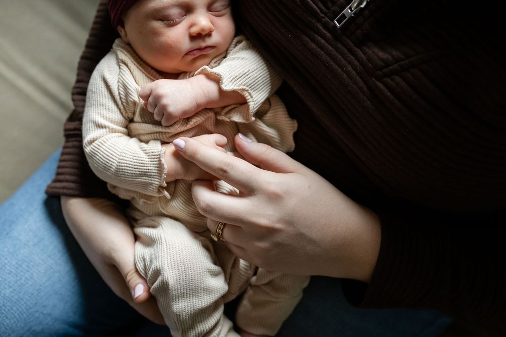 Intimate sequence of a sleeping infant wearing a cream colored sweater held in gentle embrace.