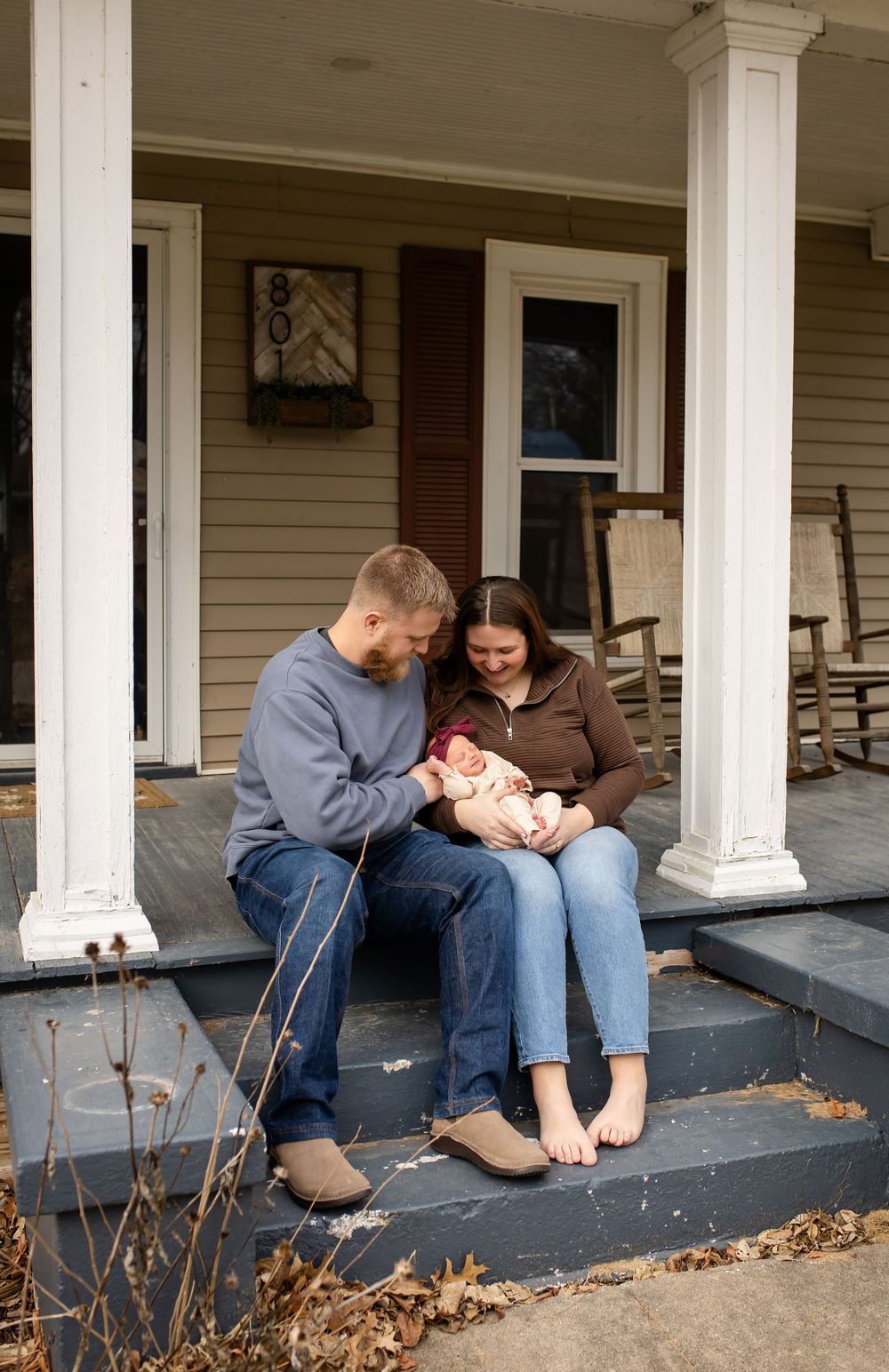 Family sitting together on a front porch with white columns surrounded by fallen autumn leaves.