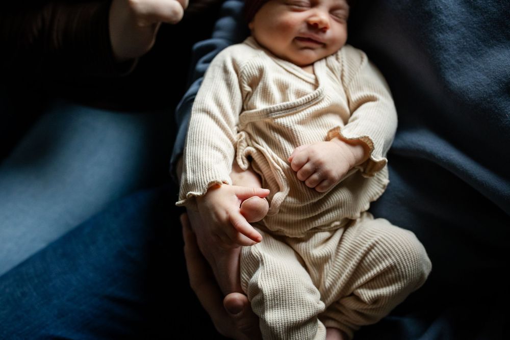 A baby in a cream-colored knit outfit lies on a dark blue background while being gently held.