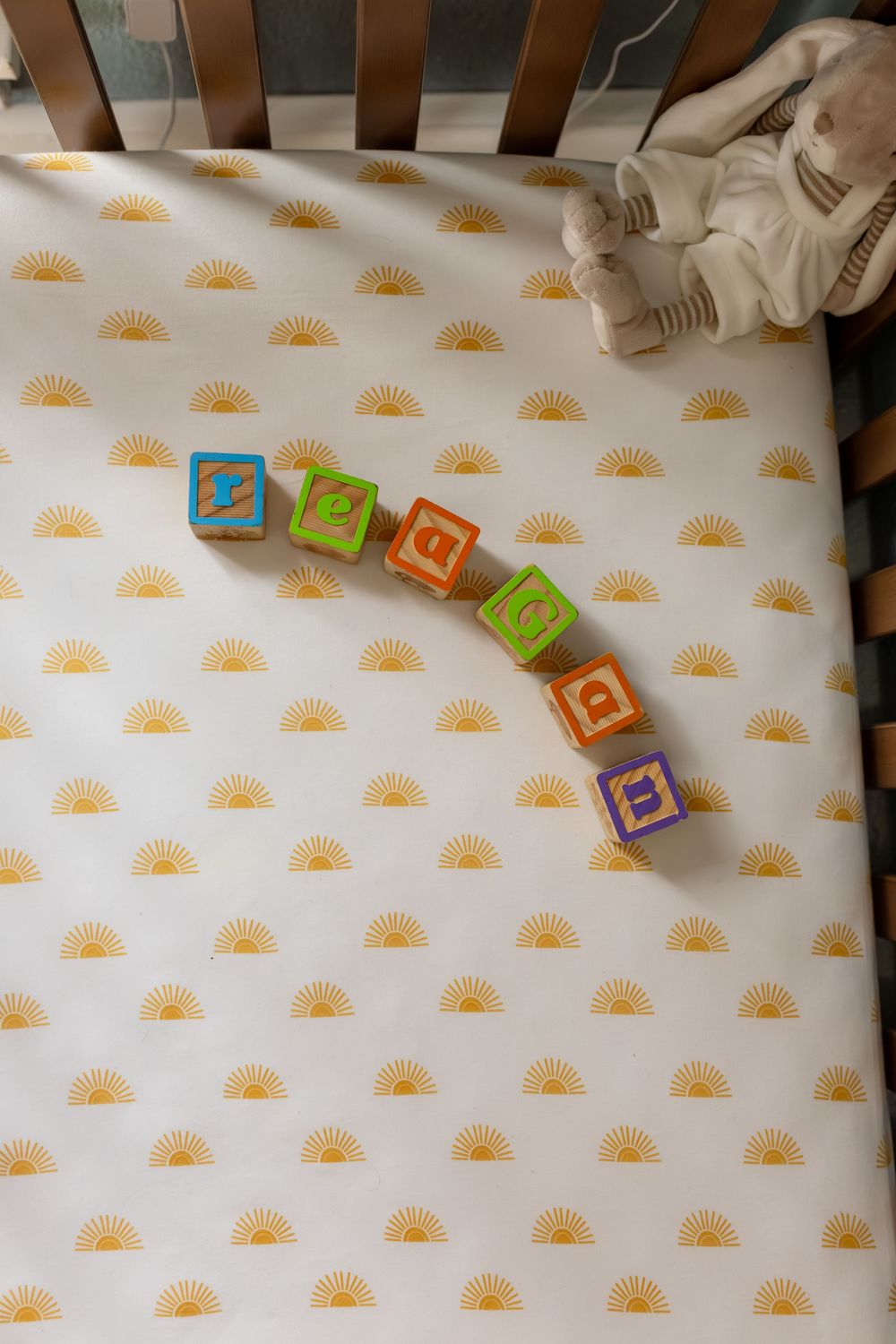 Colorful alphabet toy blocks arranged in a curved line on a white surface with small orange sun pattern design.