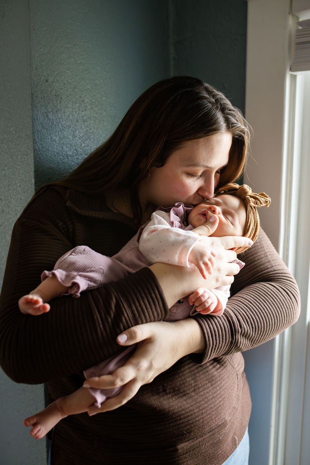 A tender moment between parent and baby in natural window light, wearing brown and pink clothing.