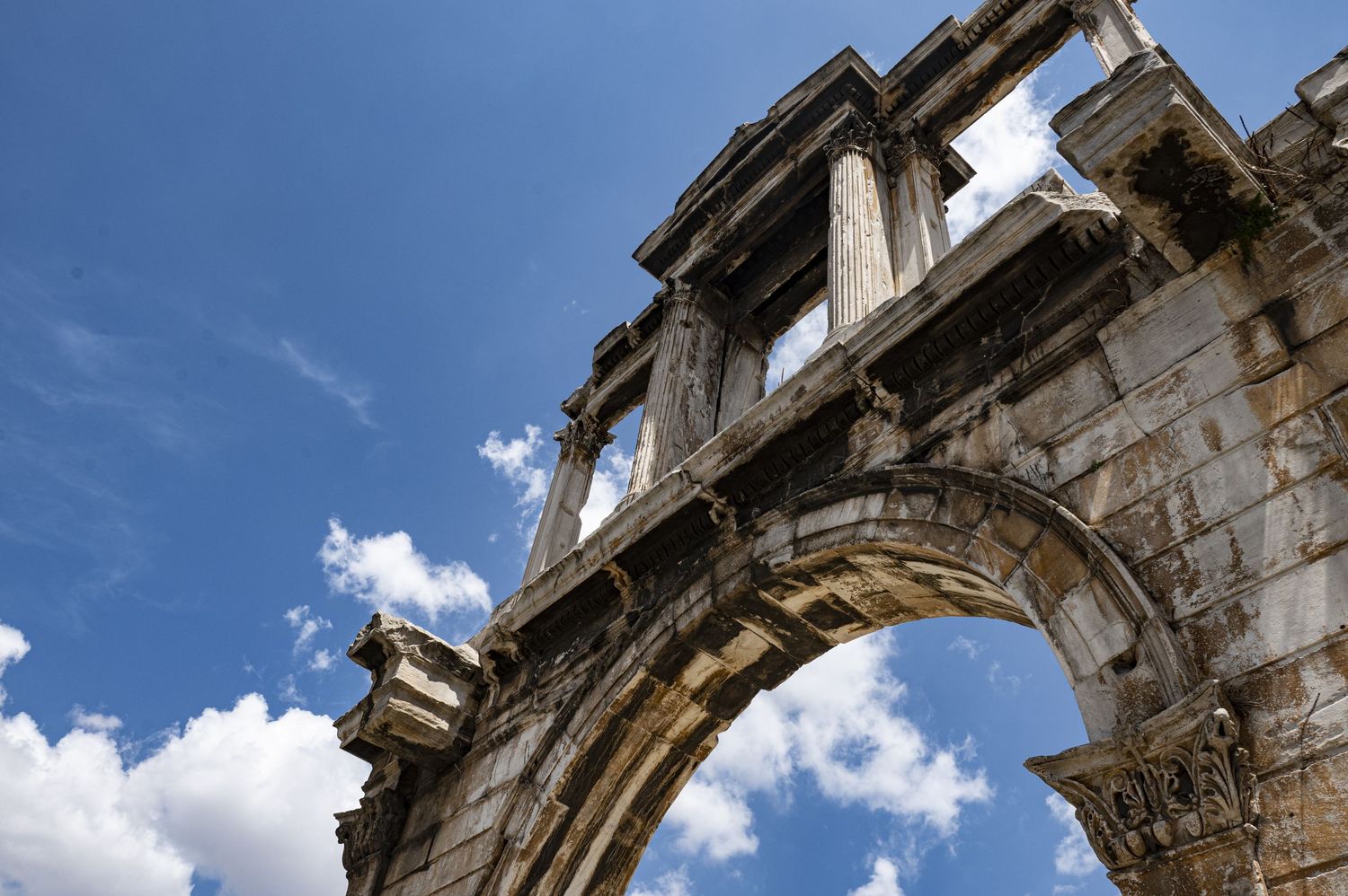Ancient stone archways and architectural details of a historic building photographed against a bright blue sky with clouds.