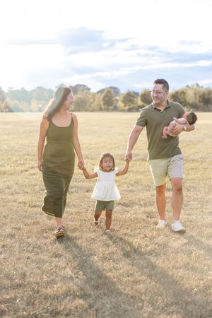 Family walking together in a golden field during sunset, holding hands and enjoying a tender moment outdoors.