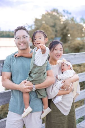 A family in coordinating teal and white outfits shares joyful moments together on a wooden fence walkway.