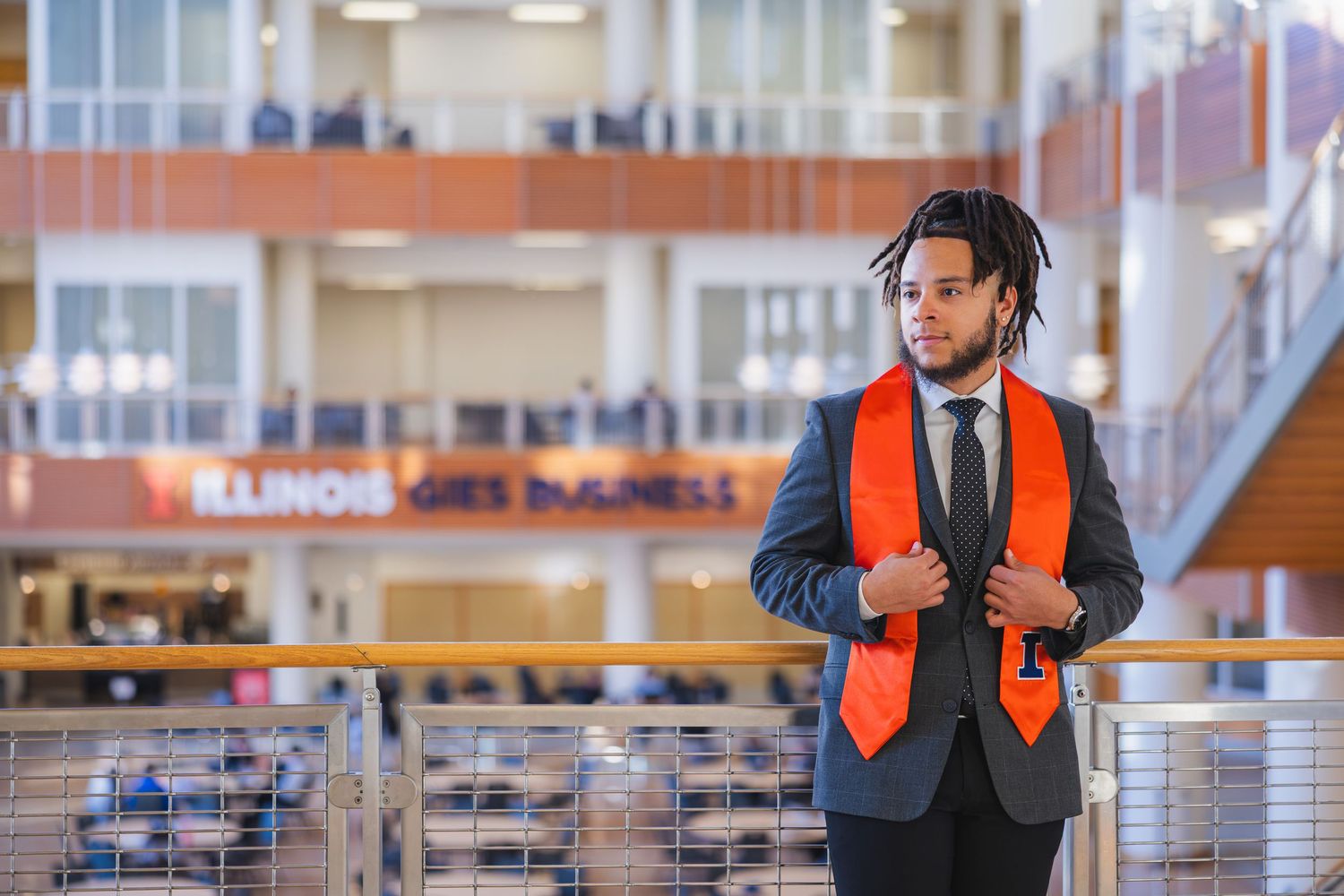 UIUC graduate with a suit and stole on the Gies College of Business balcony