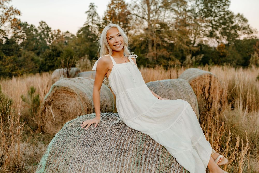 A flowing white dress contrasts against rustic rocks in a golden field during sunset.