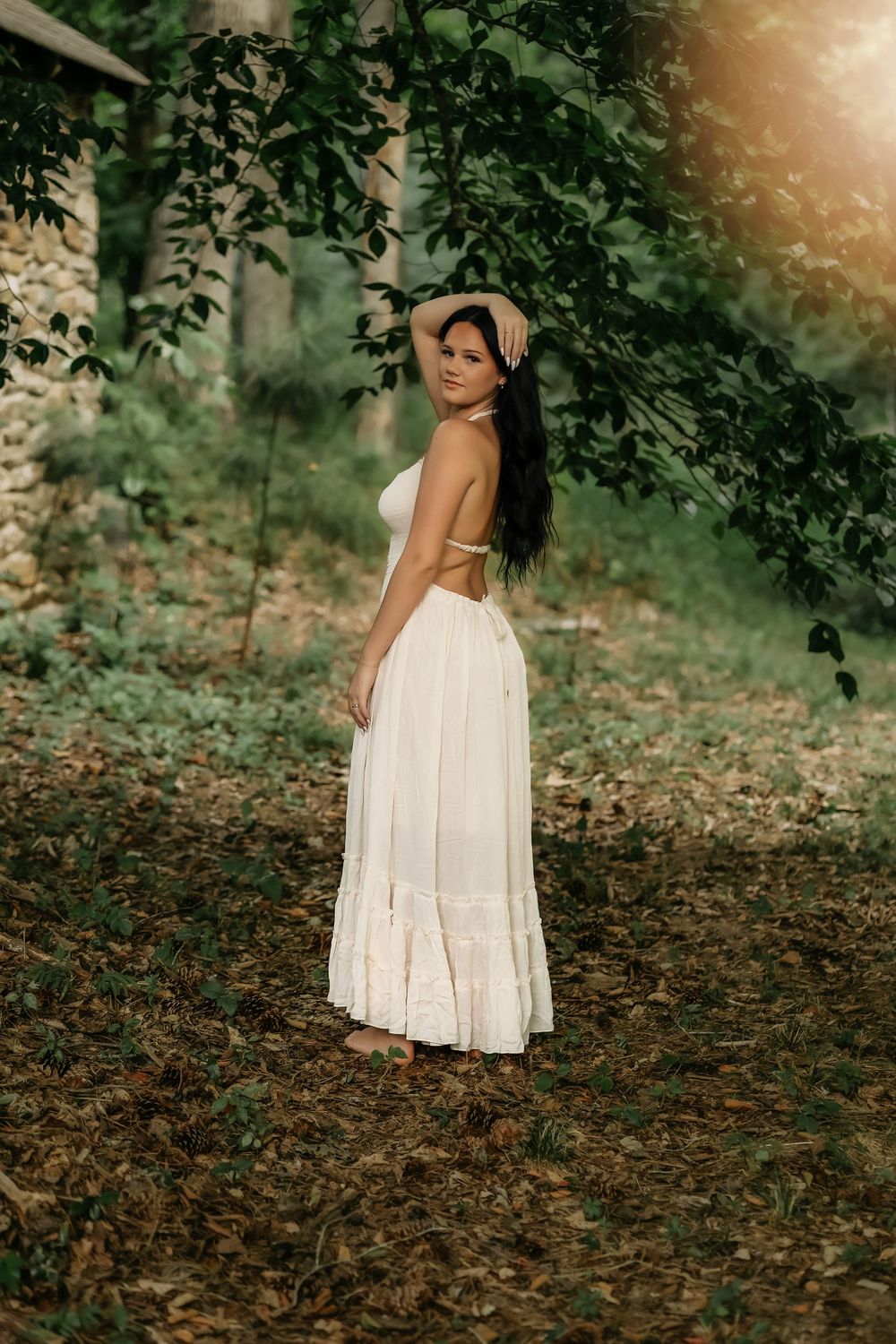 A flowing white sundress twirls gracefully against a dreamy forest backdrop with fallen leaves and filtered sunlight.