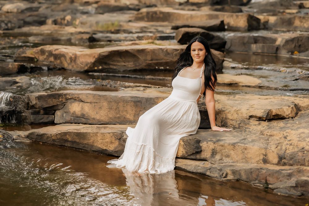 A white flowing dress contrasts against rugged rocks as water flows around the natural stone formations at sunset.