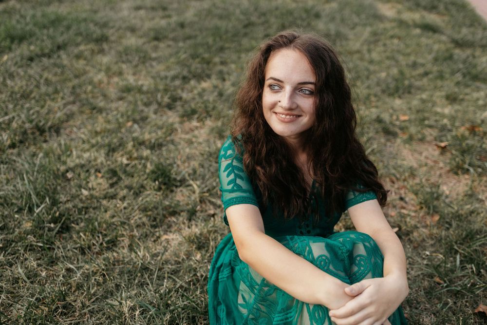 A person in a green dress poses outdoors in a natural setting during a photo session.