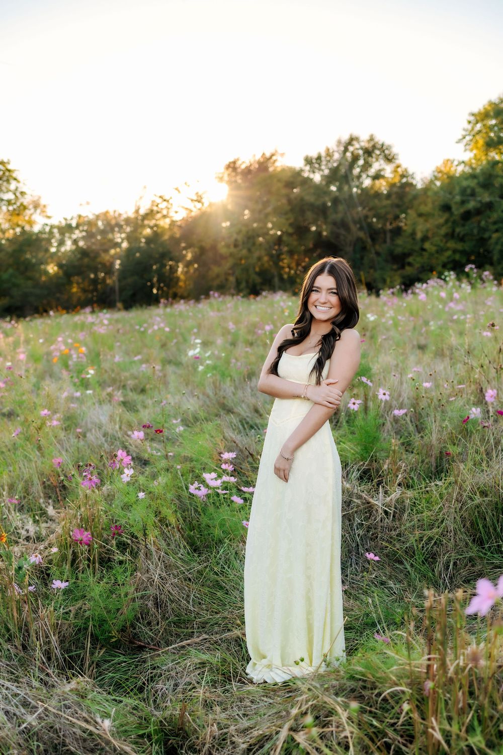 Soft yellow dress flows in a summer meadow filled with pink cosmos flowers at sunset.