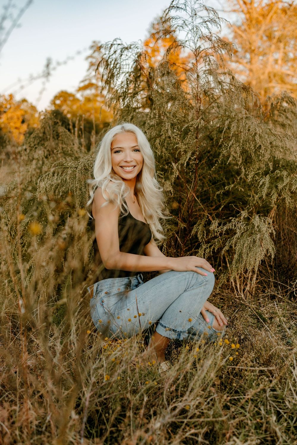 Golden hour outdoor portrait amidst tall wild grasses and autumn trees.