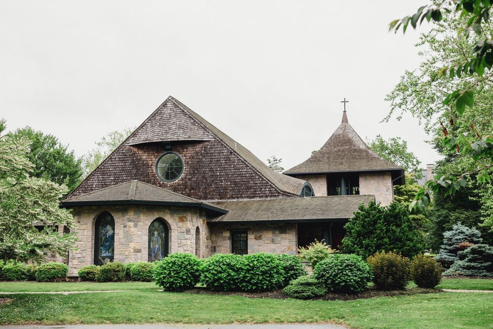 Stone church building with unique round architecture and turret surrounded by lush landscaping and trees.